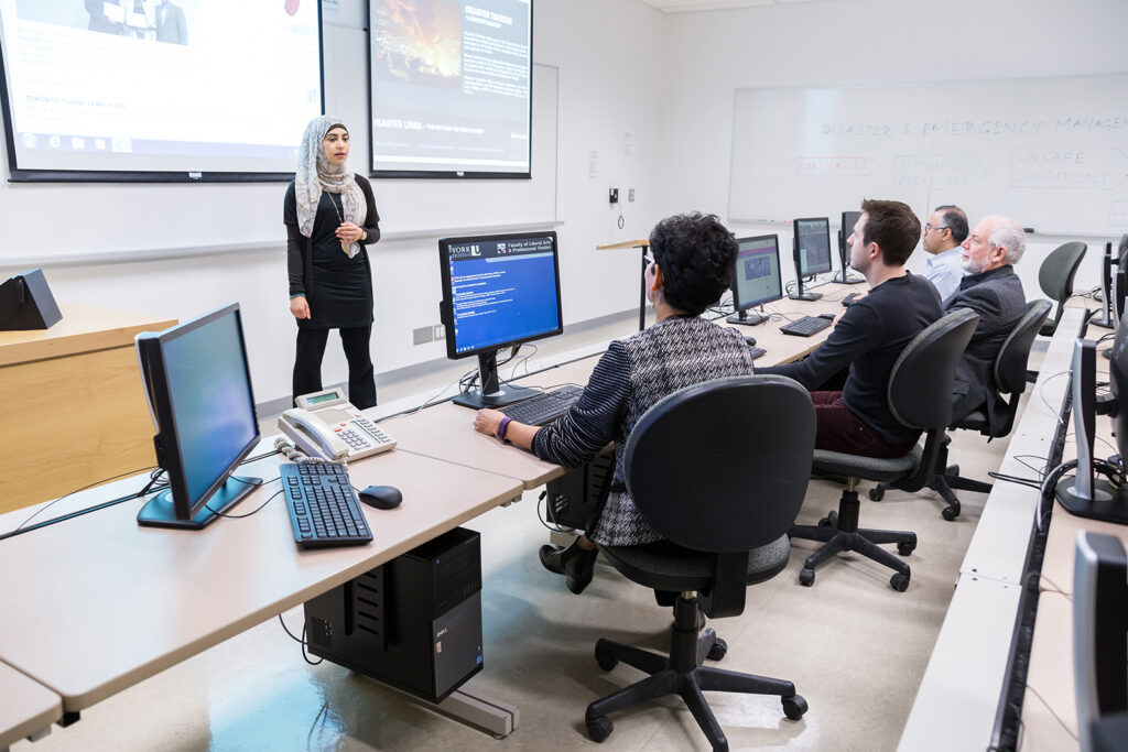 an instructor at the front of a computer lab teaching to students at computers