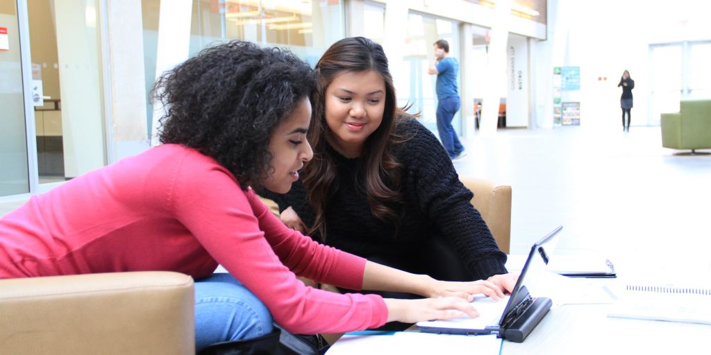 Two students work on a laptop computer.