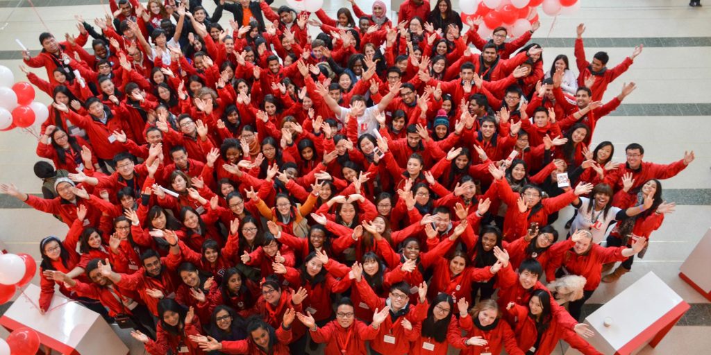 An overhead shot of a large group of students with their hands in the air.