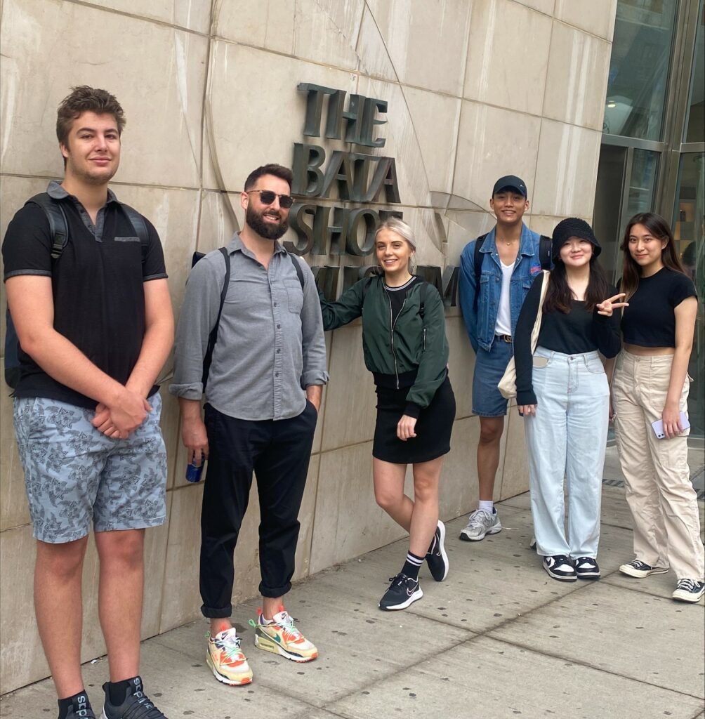 This is an image of a teacher with 5 students standing in front of the Bata Shoe Museum sign outside of the museum.