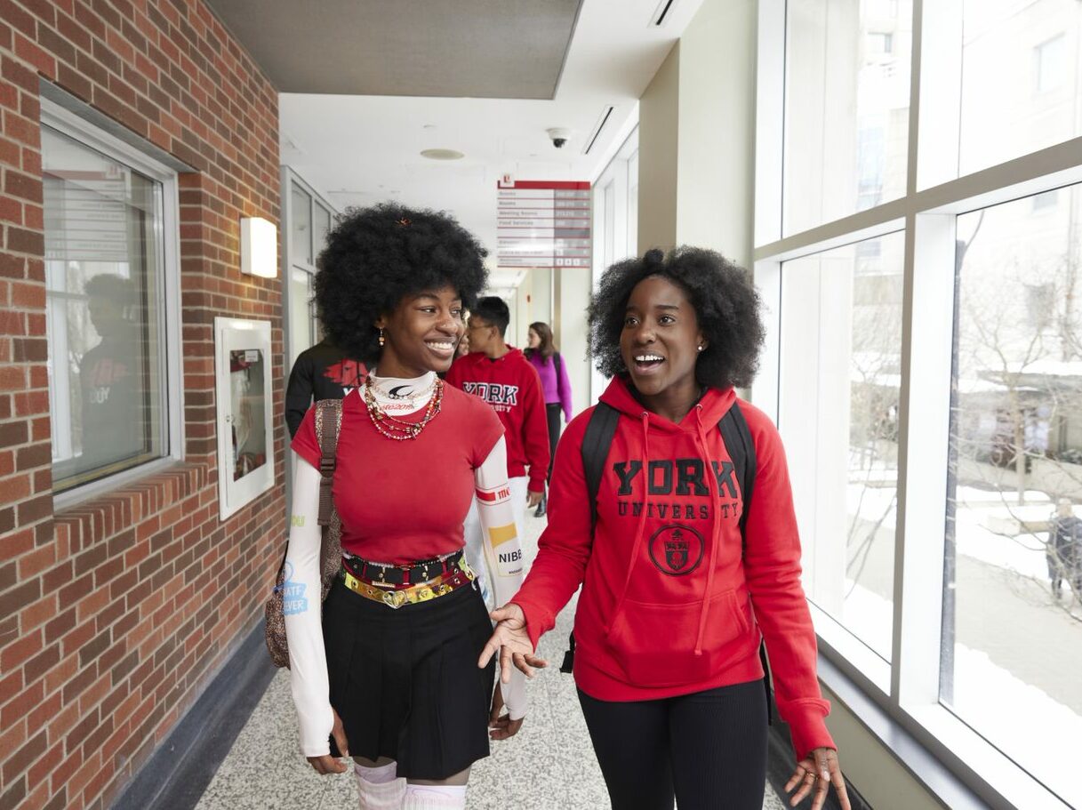 Two students walking down a brightly-lit hall engaged in a happy conversation.
