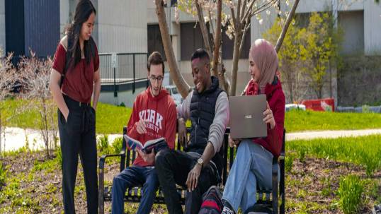 Students sitting on a bench, talking on the campus walk.