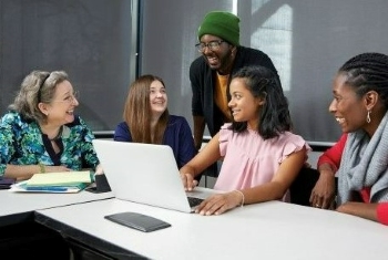 Students and professor smiling while working together on a laptop.