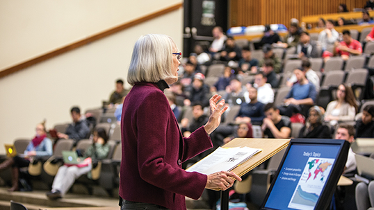 A professor stands at a lectern in a hall