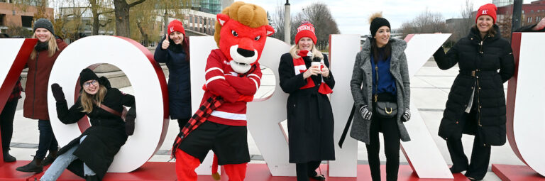 Rhonda Lenton with Yeo and students in front of the York U letters at winter