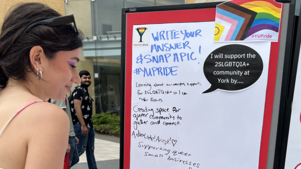 Female student looking at stand up board with @SLGBTQIA+ resources