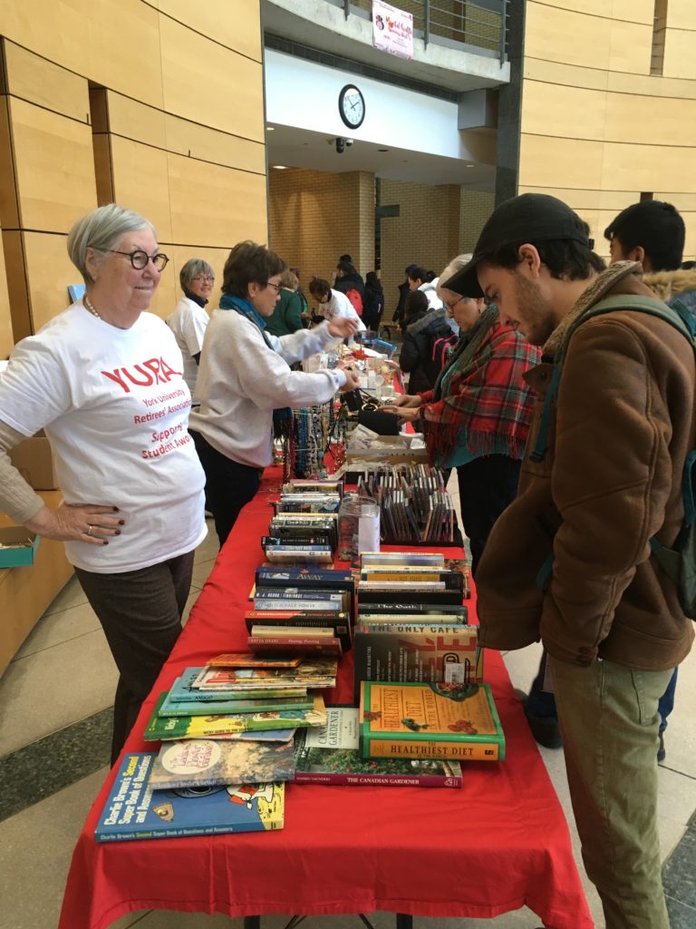 Image of the Showcase "book and DVD" table in the Vari Hall Rotunda with YURA volunteers and buyers flanking the table